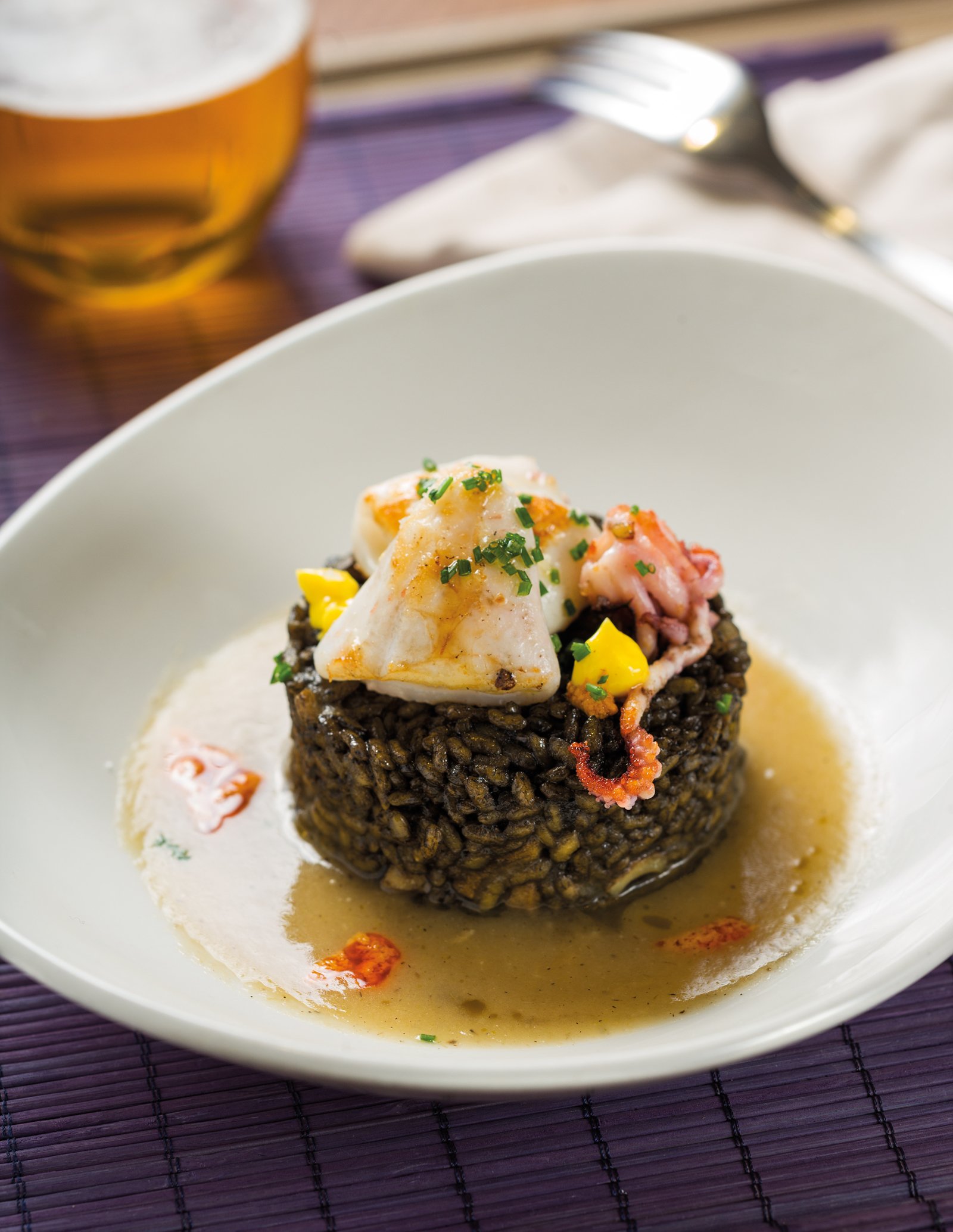 Arròs negre amb crema de calçots i calamarsons, puntets d'allioli de safrà i romesco